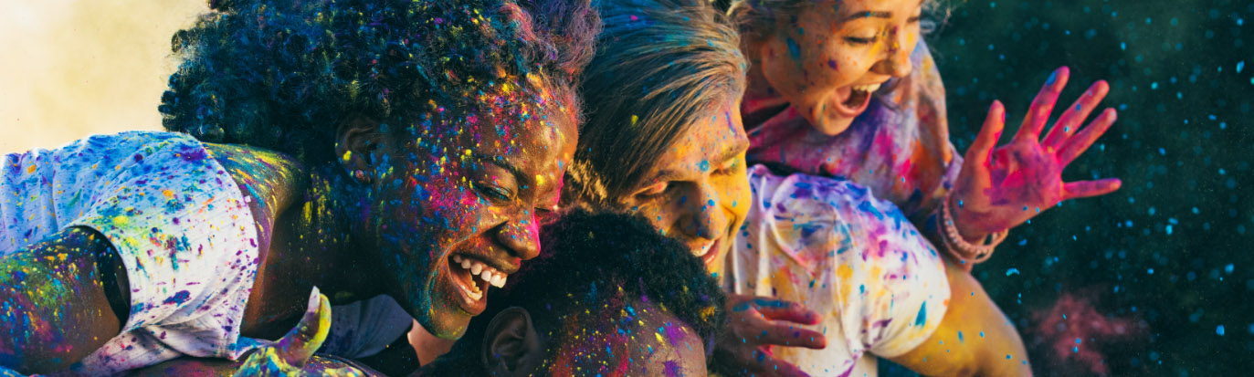 A group of young people laughing with colourful powder on their faces and hands