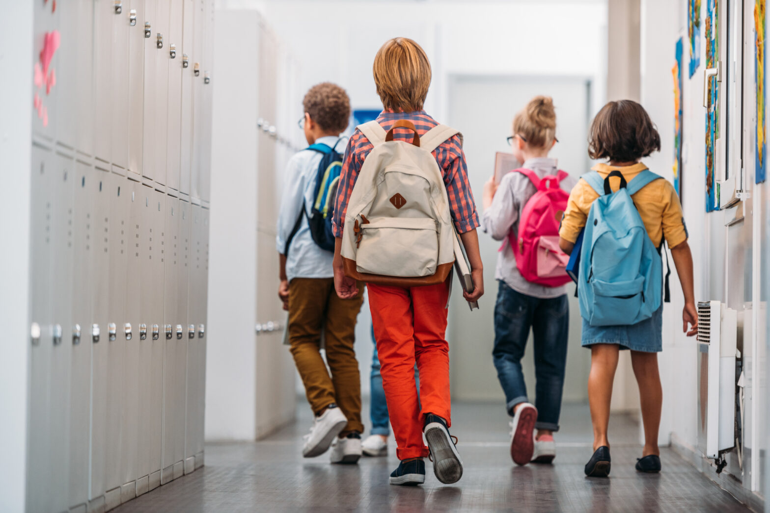 A group of children walking through a corridor with bagpacks