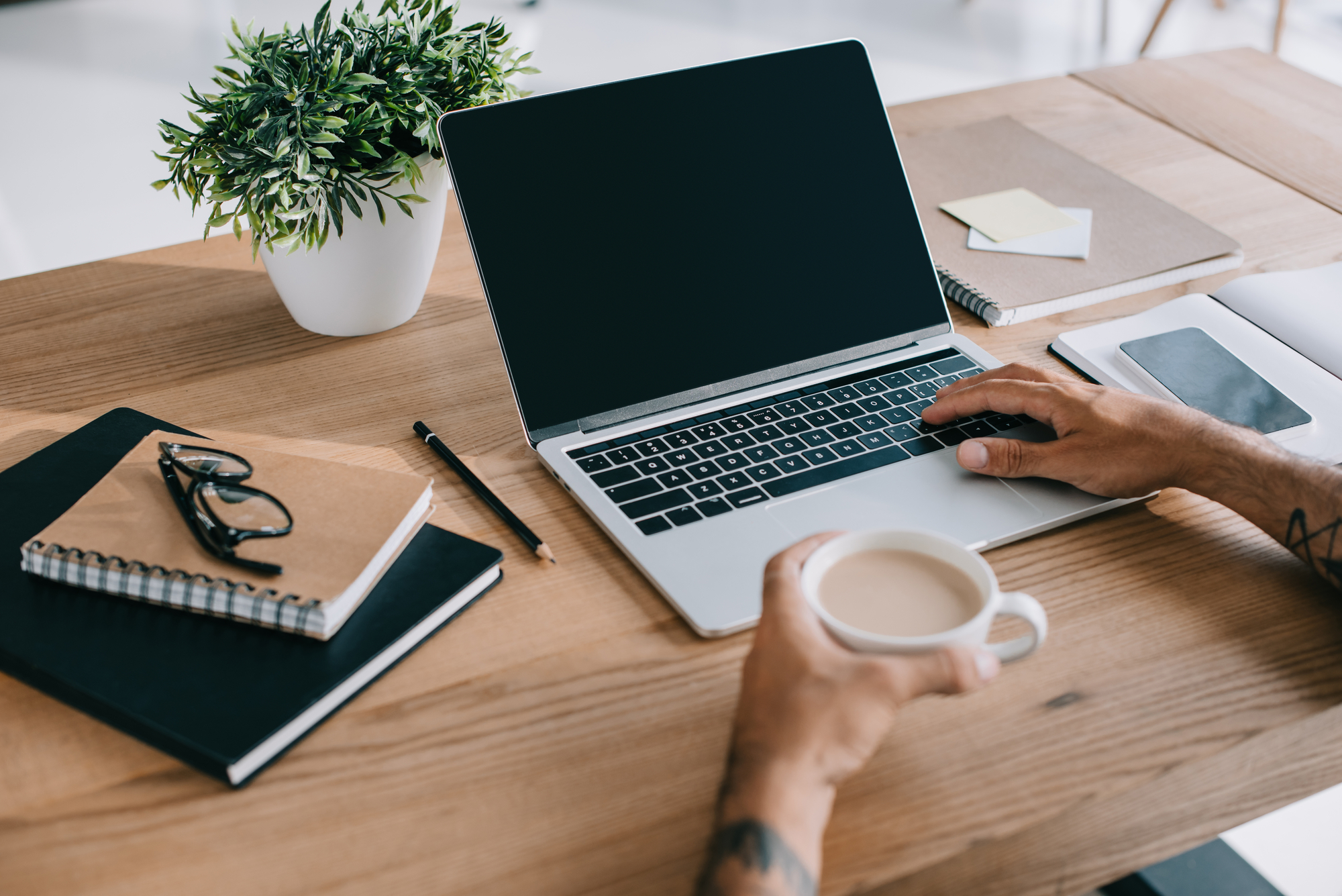 Cropped view of man using laptop with blank screen and holding cup of coffee