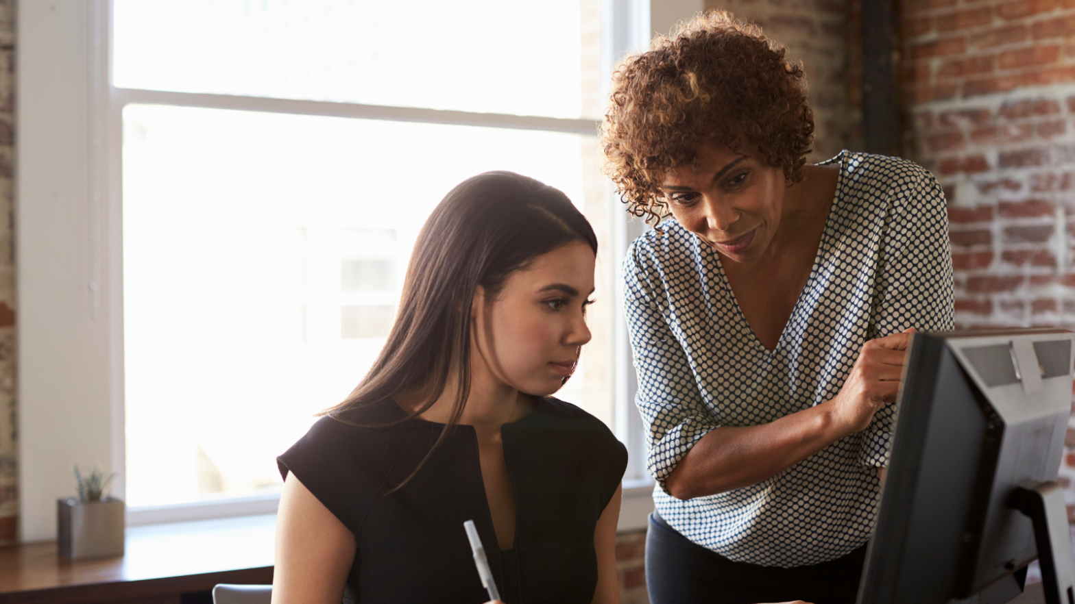 A stock image of an educator and a student looking at a computer screen, discussing a project